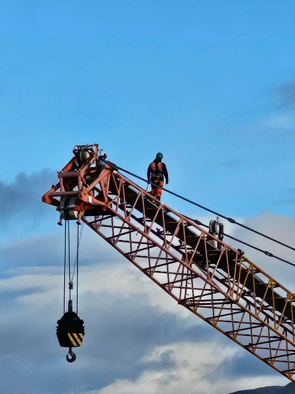 Competent person inspecting a crane lattice jib at height against the sky